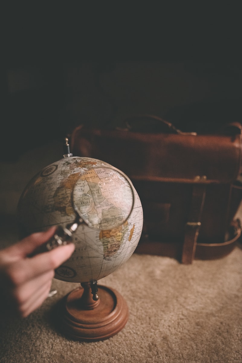 Photo par Clay Banks person holding magnifying glass near desk globe